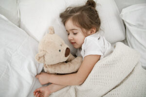 A cute little girl is sleeping in a bed with a Teddy bear toy .